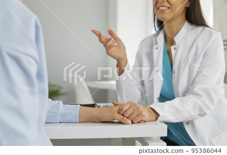 Caring physician is talking to a young woman, supporting her and holding her hand 95386044