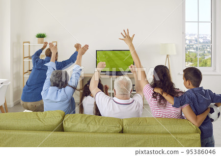 Back view of happy family sitting on sofa at home and watching football match on TV 95386046