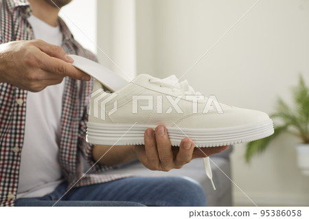 Young man puts new orthotic insoles inside his comfortable white orthopedic shoes 95386058