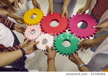 Creative young people hold colored gears of different sizes symbolizing coordinated teamwork. Creative young people hold colored gears of different sizes symbolizing coordinated teamwork. 95386088