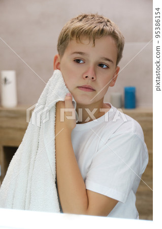 Reflection of schoolboy wiping his face with a towel after washing in bathroom. 95386154