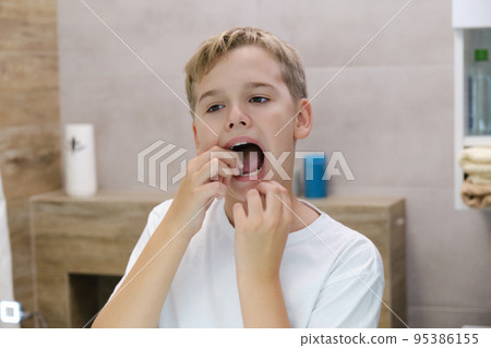 Close up head shot mirror reflection of a happy boy flossing his teeth. 95386155