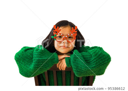 Cute asian child girl in green sweater and masquerade christmas glasses with deer horns Cute asian child girl in green sweater and masquerade christmas glasses with deer horns 95386612