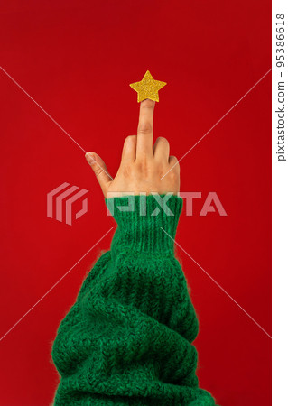 Hand in green sweater, middle finger with star raised up, abstract symbol of Christmas tree 95386618