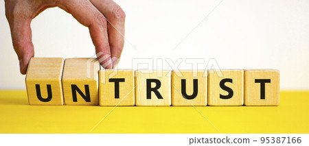 Untrust or trust symbol. Businessman turns wooden cubes, changes words 'untrust' to 'trust'. Beautiful yellow table, white background. Business and untrust or trust concept, copy space. Untrust or trust symbol. Businessman turns wooden cubes, changes words 'untrust' to 'trust'. Beautiful yellow table, white background. Business and untrust or trust concept, copy space. 95387166