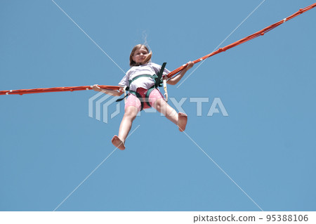 Little girl bouncing high in the air using a bungee trampoline Little girl bouncing high in the air using a bungee trampoline 95388106
