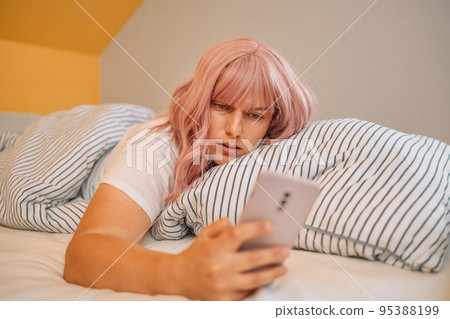 Shocked young woman laying in bed and looking at alarm at smartphone in bedroom at home. 95388199