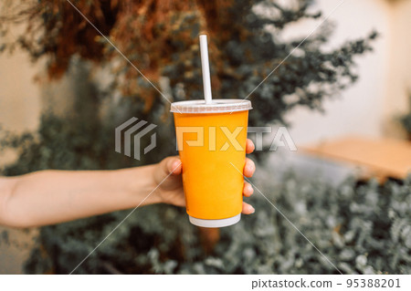 Woman hand holding plastic cup with drink at city street Woman hand holding plastic cup with drink at city street 95388201