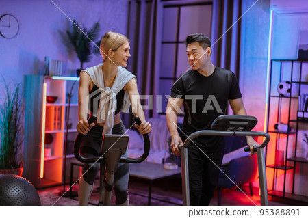 Home fitness workout sporty people training on exercise machines indoors at evening time. Home fitness workout sporty people training on exercise machines indoors at evening time. 95388891