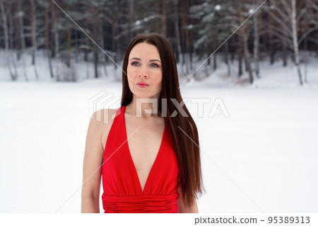 beautiful brunette girl in a thin red dress and barefoot in the winter forest 95389313