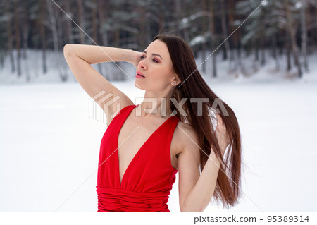 beautiful brunette girl in a thin red dress and barefoot in the winter forest 95389314