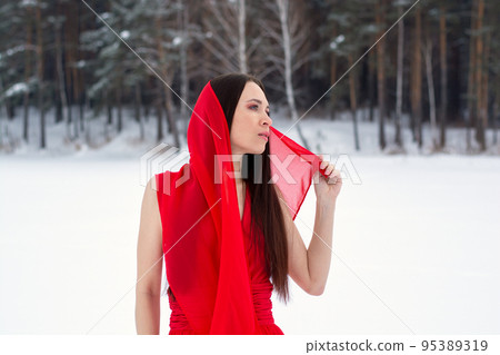 beautiful brunette girl in a thin red dress and barefoot in the winter forest 95389319