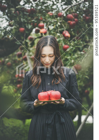 A woman in a black dress holding an apple in an orchard A woman in a black dress holding an apple in an orchard 95389521