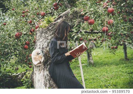 A woman in a black dress reading in an orchard A woman in a black dress reading in an orchard 95389570