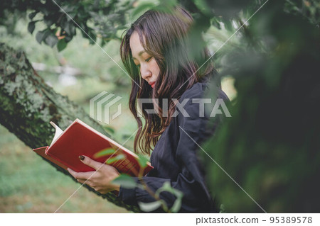 一個穿著黑色連衣裙的女人在果園裡看書 一個穿著黑色連衣裙的女人在果園裡看書 95389578