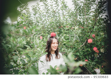 一個穿著白色連衣裙的女人拿著一個蘋果 95389683