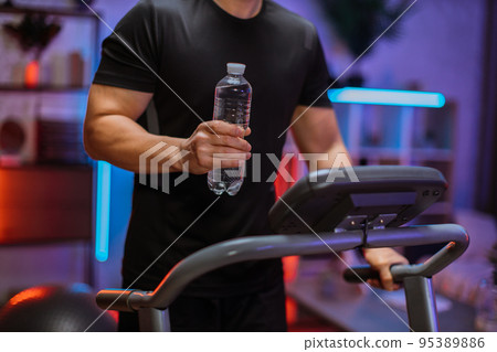 Focus on water bottle of asian man, working out, running, doing cardio training on treadmill 95389886