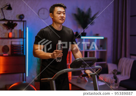 Attractive asian man with water bottle working out, running, doing cardio training on treadmill Attractive asian man with water bottle working out, running, doing cardio training on treadmill 95389887