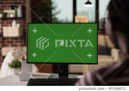 Computer with green screen in freelancer home office, selective focus on pc monitor mock up. Woman working, sitting at workplace desk, employee professional equipment with chroma key display 95390012