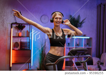 Happy young caucasian female athlete jogging on treadmill at home. 95390255
