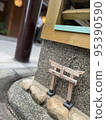 A small torii gate placed at the corner of the sidewalk 95390590
