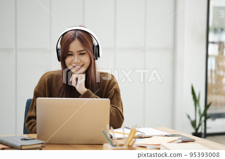 Young woman studying or working online using laptop and wearing headphones. Young woman studying or working online using laptop and wearing headphones. 95393008