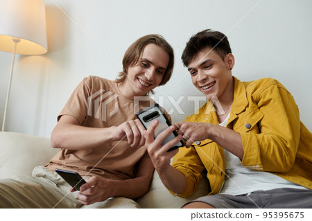 Joyful young men discussing new mobile application they download on smartphone Joyful young men discussing new mobile application they download on smartphone 95395675