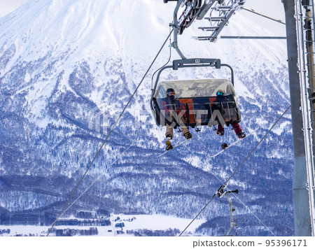 Snowboarders riding lifts with Mount Yotei in the background (Niseko, Hokkaido) Snowboarders riding lifts with Mount Yotei in the background (Niseko, Hokkaido) 95396171