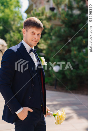 the groom is in a dark blue suit with a boutonniere and a bouquet of callas. the groom is in a dark blue suit with a boutonniere and a bouquet of callas. 95396550