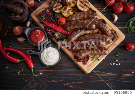 Grilled sausages and vegetables on wooden cutting board at domestic kitchen Grilled sausages and vegetables on wooden cutting board at domestic kitchen 95396990