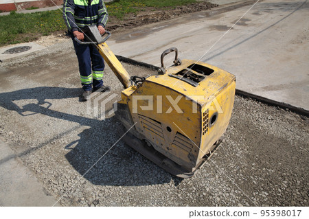 Worker use vibratory plate compactor at road construction site 95398017
