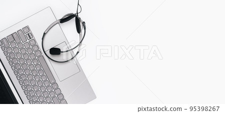 Top view of slim laptop with headset on white desk. Monochrome background. Distant learning. working from home, online courses or support. Audio podcast headphones . Helpdesk or call center banner 95398267