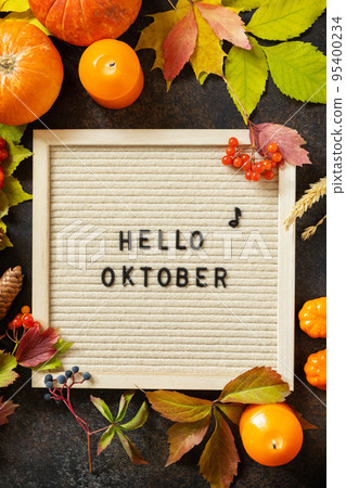 Autumn background with Hello October letters and autumn message board, pumpkins and colorful leaves. Cozy autumn mood. Fall seasons greeting card. 95400234