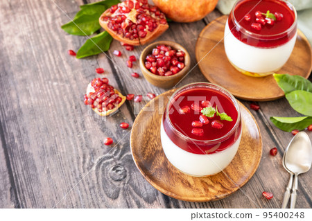Winter delicious italian dessert panna cotta with pomegranate jelly and mint, homemade cuisine on a wooden background. Copy space. 95400248