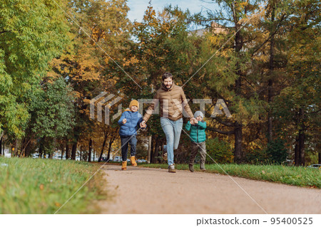 father and sons running along the autumn park holding hands. Family day concept 95400525