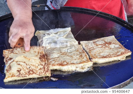 Person cooking murtabak on pan at street market during muslim iftar season Person cooking murtabak on pan at street market during muslim iftar season 95400647