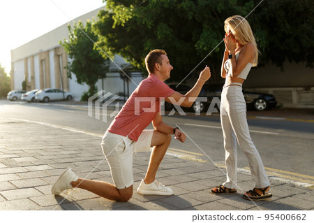 Young man with engagement ring making proposal to his beloved girlfriend outdoors.  95400662