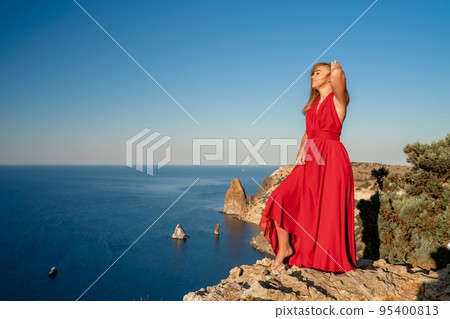 A woman in a red flying dress fluttering in the wind, against the backdrop of the sea. 95400813