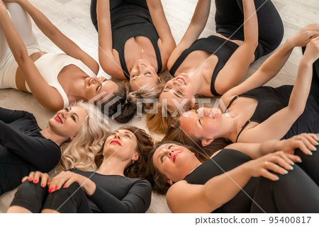 Seven happy women lie on their backs on the floor with their hea 95400817