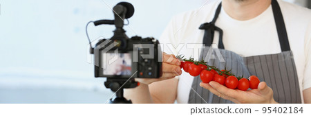 Vlogger chef showing ripe tomatoes ingredient, man in apron recording red vegetable 95402184