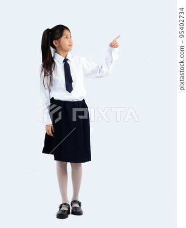 Asian junior school girl student in british formal uniform posing finger pointing and touching on white background full body length. Back to school.. 95402734