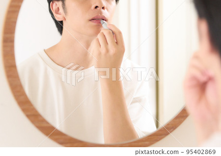 A man applying lipstick in front of a mirror Men's beauty image 95402869