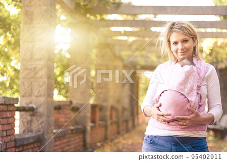 Beautiful Young mother carrying a newborn baby in a pink shawl sling in a sunny day- Concept Young Mothers. 95402911