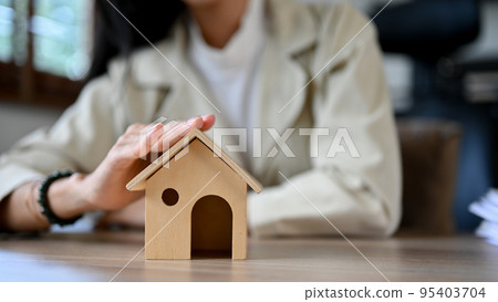 Close-up, A female real estate agent or home insurance broker touching a house's roof model 95403704