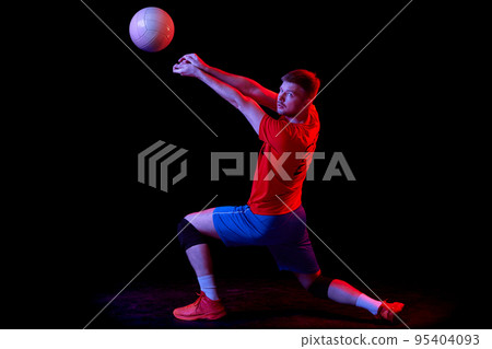 Dynamic portrait of male volleyball player training with ball isolated on dark background in neon light. Sport, gym, team sport, challenges 95404093