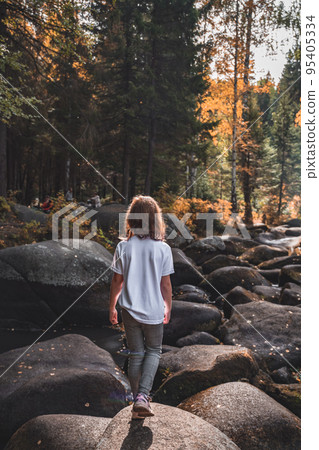 a girl walks on the stones of the river in autumn a girl walks on the stones of the river in autumn 95405334