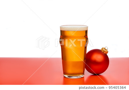 Pint glass of ale or beer with christmas bauble on red background Pint glass of ale or beer with christmas bauble on red background 95405364