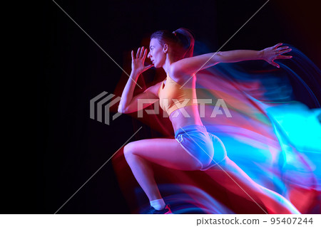 Speed. Professional female athlete, runner in motion over dark background in mixed neon light. Art, beauty, sport, cyberpunk concept Speed. Professional female athlete, runner in motion over dark background in mixed neon light. Art, beauty, sport, cyberpunk concept 95407244