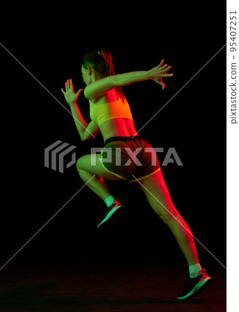 Professional female athlete running isolated on dark background in neon light. Healthy lifestyle, skills, sport, fitness, speed and energy concept. 95407251