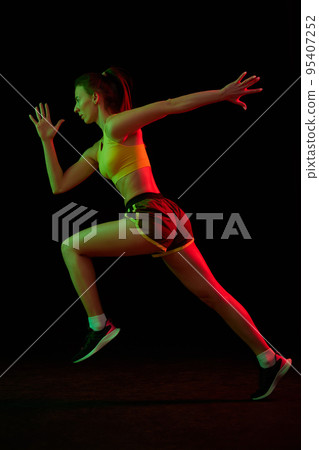 Running technique. Professional female jogger running isolated on dark background in neon light. Sport, fitness, speed and energy concept. Running technique. Professional female jogger running isolated on dark background in neon light. Sport, fitness, speed and energy concept. 95407252